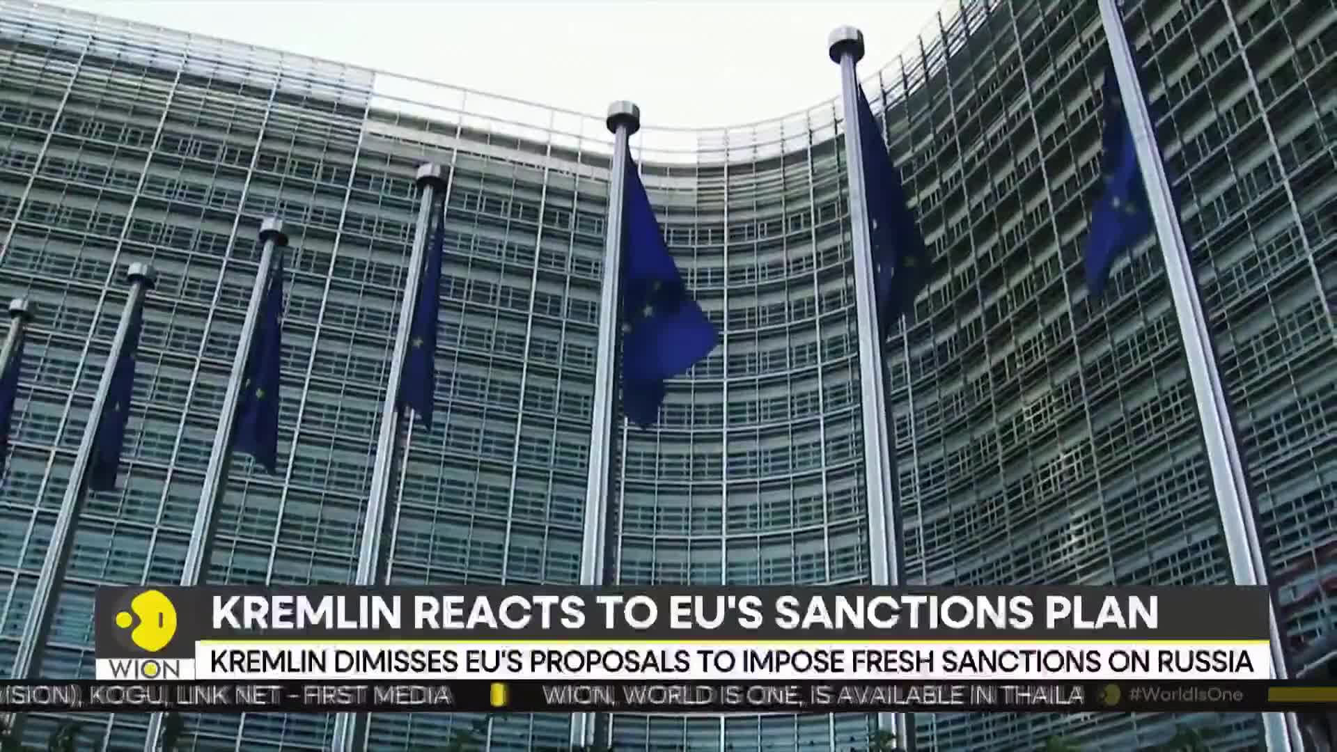 Blue flags with golden stars hang limply on tall poles in front of a modern, glass-walled building. The WION logo and a headline about sanctions are visible at the bottom of the screen.

