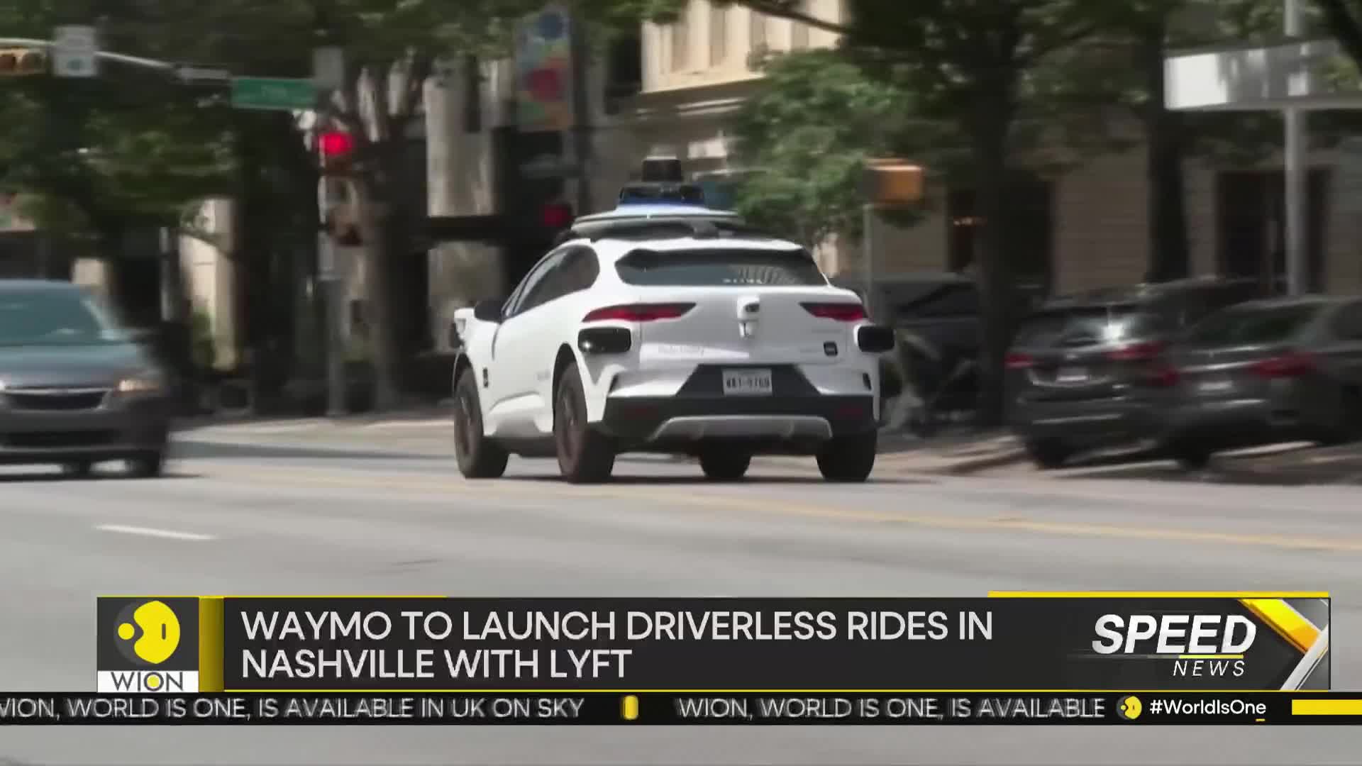 A white car, equipped with sensors on its roof, cruises down the street. The WION news ticker at the bottom announces the launch of driverless rides in Nashville.
