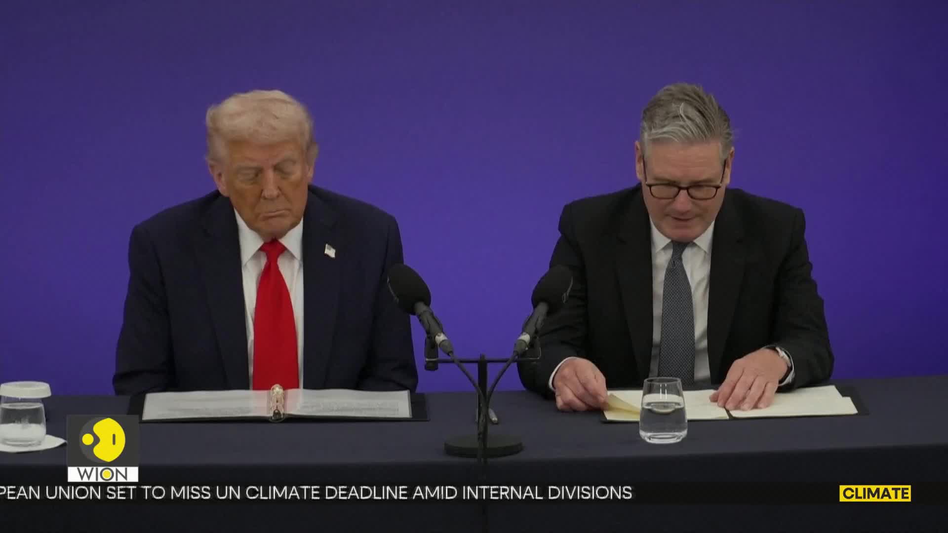 The man on the left stares down, his eyes closed, while the other man shuffles through papers.  A WION logo sits in the corner, and the backdrop is a solid blue.
