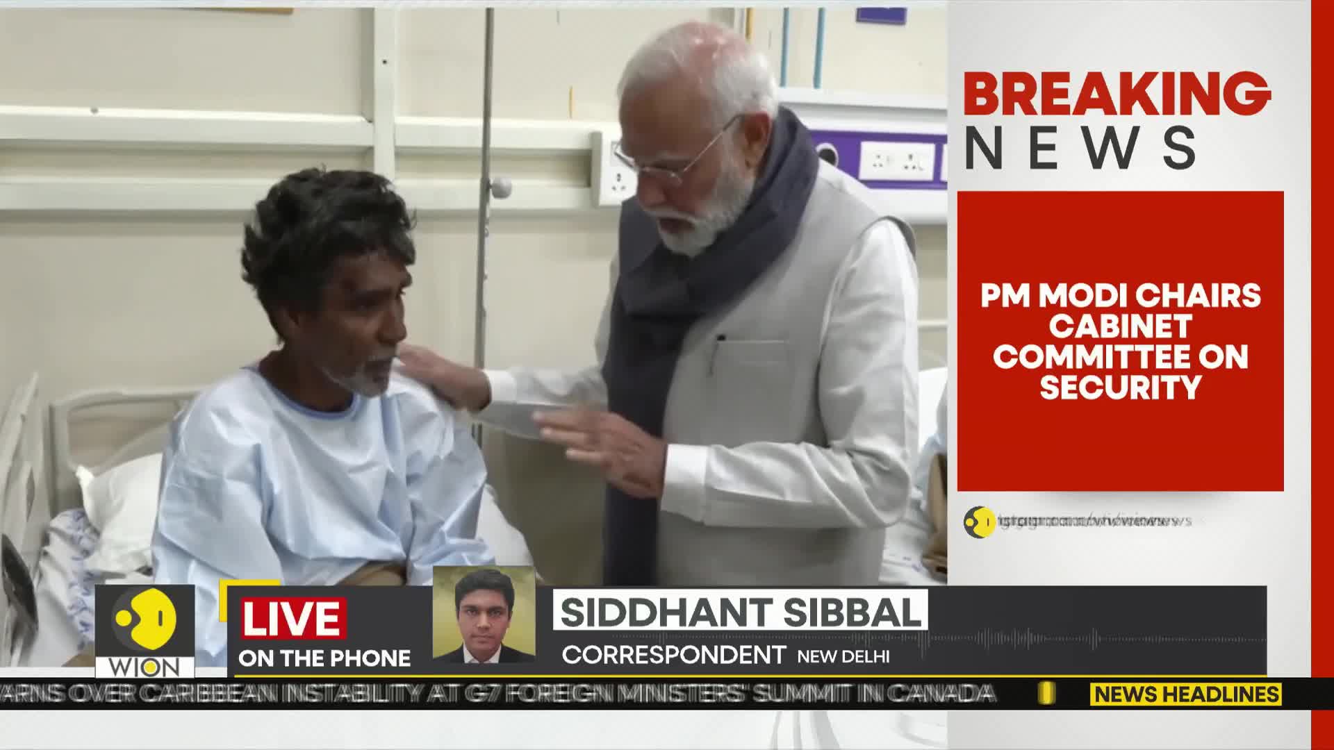 A man in a hospital bed, wearing a blue gown, is being spoken to by another man in a vest and scarf. The news ticker at the bottom of the screen mentions India and a WION correspondent.
