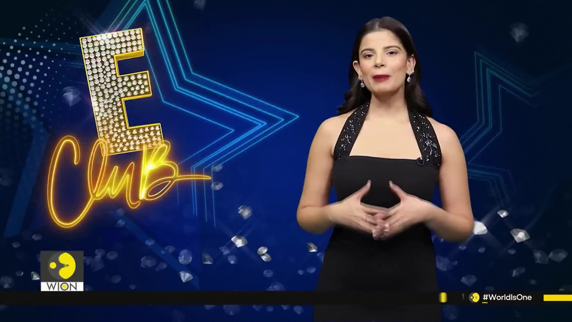 A woman in a black dress stands in front of a blue backdrop, gesturing with her hands. Behind her, a glowing "E Club" logo and the WION logo are visible.
