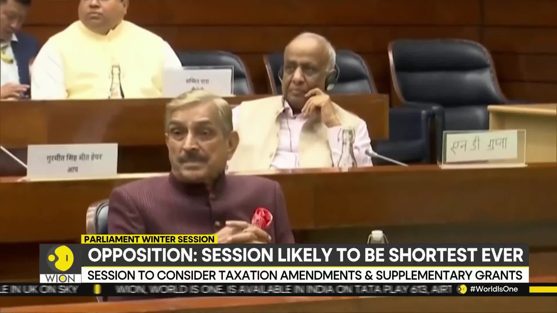 A man in a maroon jacket speaks, his gaze focused forward, while another man listens intently. The WION news banner highlights a parliamentary session in India.
