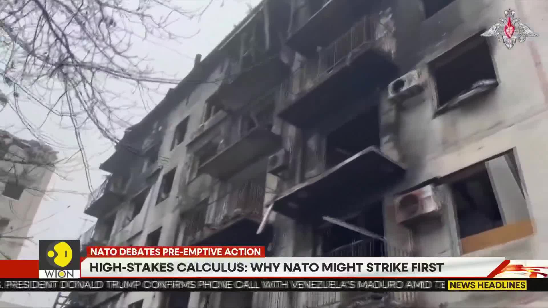 The side of a building, blackened by fire, is the main focus. Bare branches frame the scene, and a news ticker from WION runs across the bottom of the screen.
