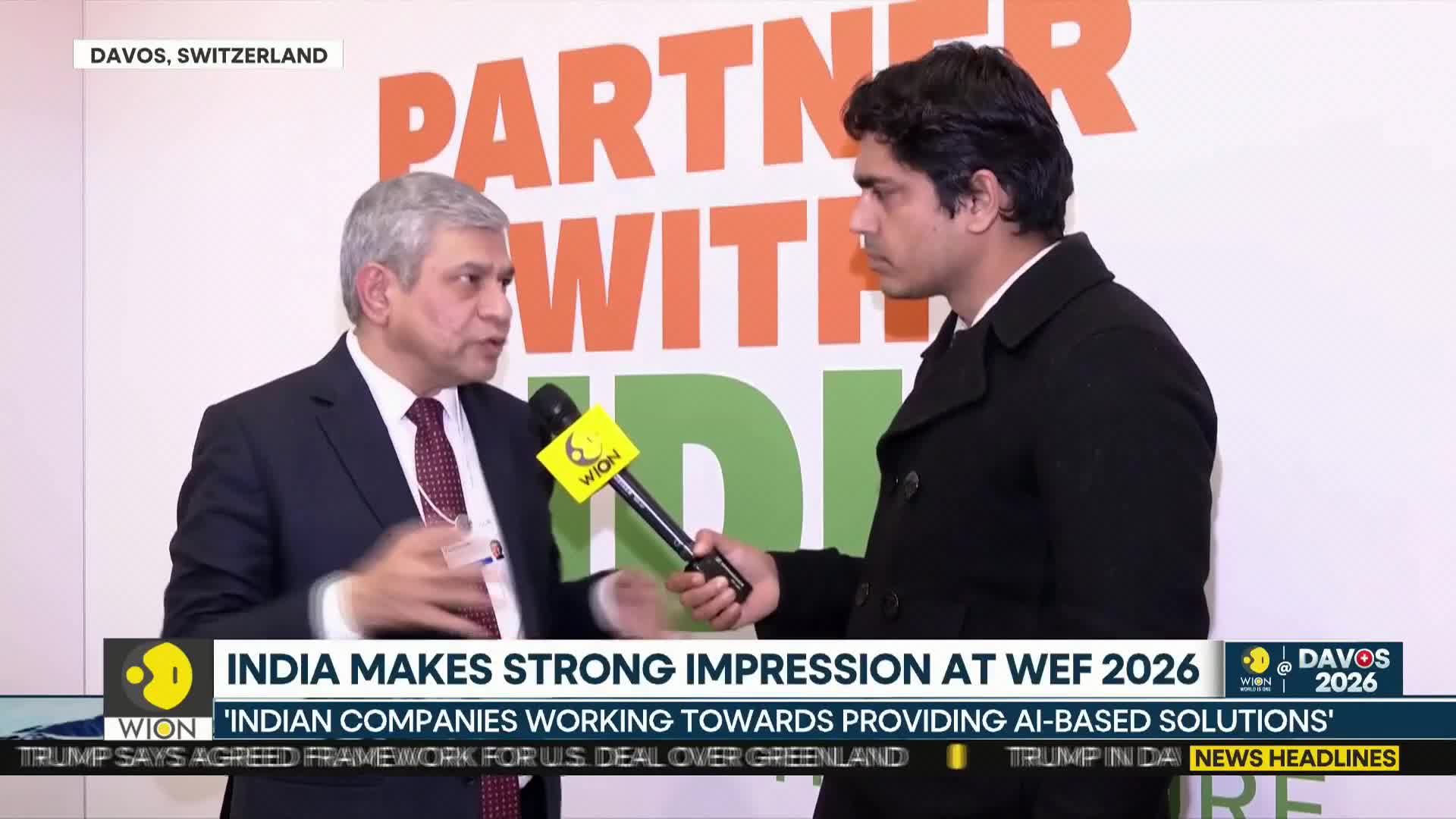 A man in a suit gestures with his hands as he speaks into a WION microphone. The reporter, dressed in a dark coat, holds the microphone steady, listening intently.