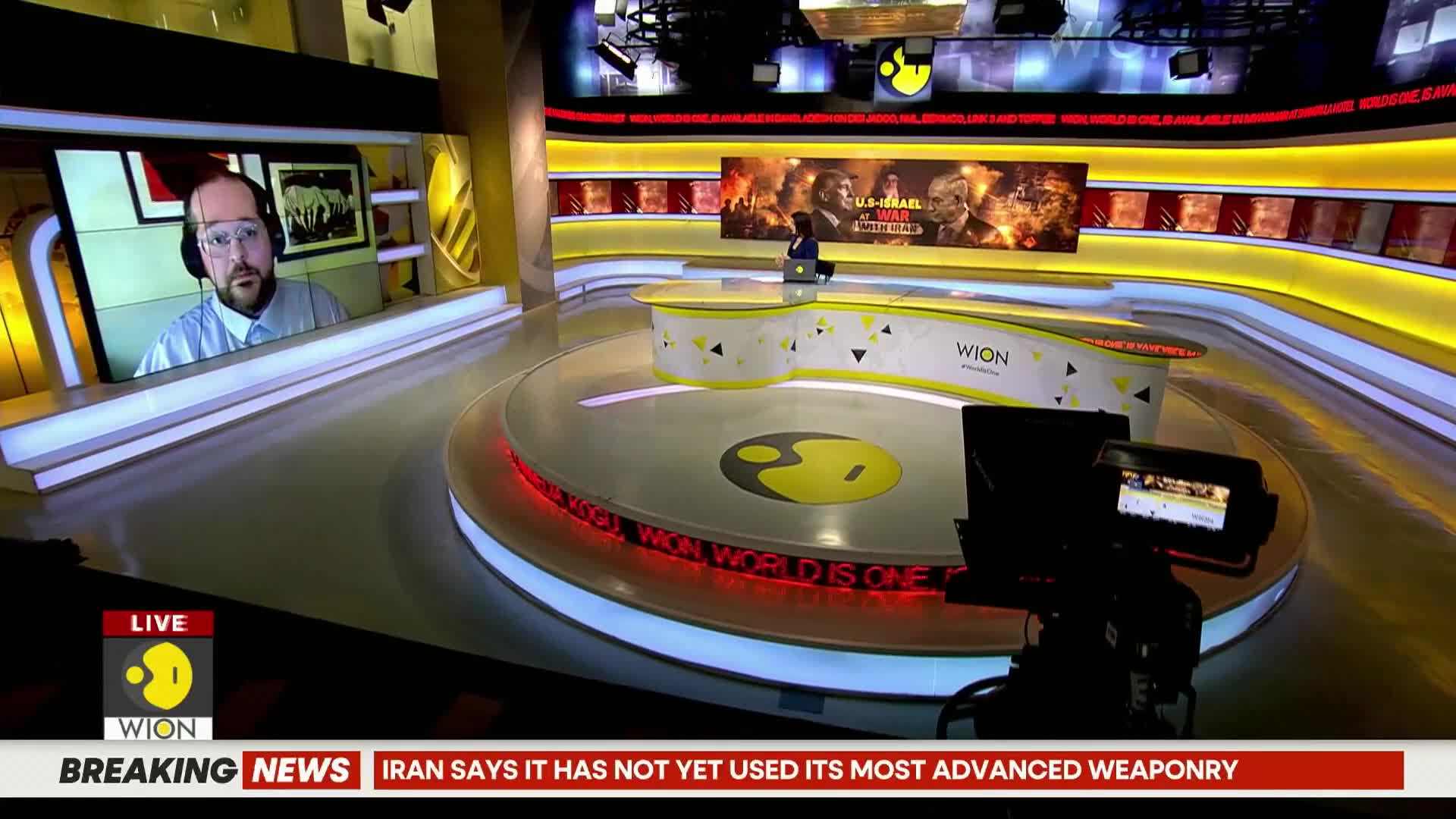 A man with glasses and headphones speaks from a screen on the left, while a woman sits at a desk in the center of the studio. The WION logo is visible on the desk and on a screen behind the woman.