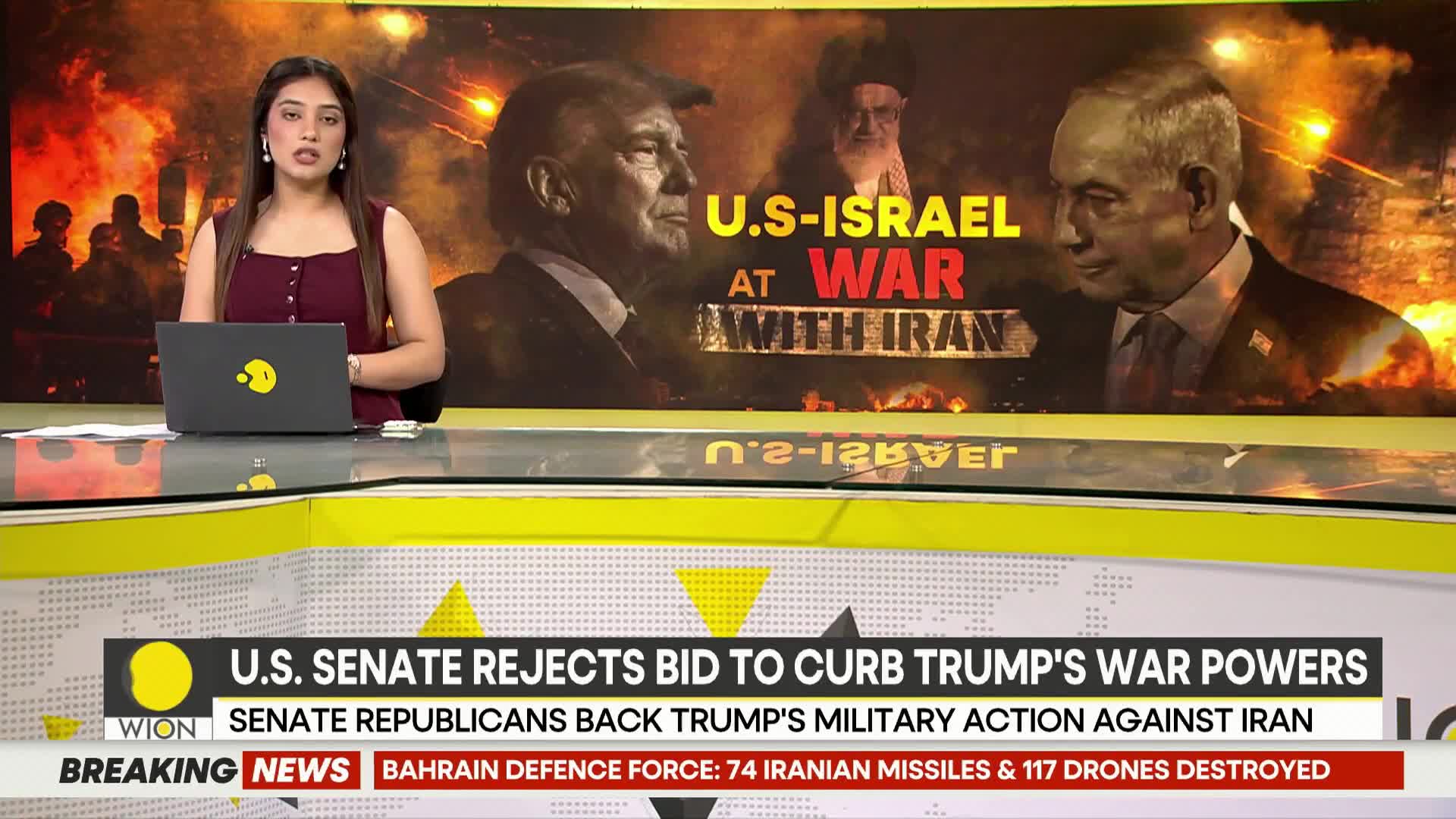 A news anchor sits at a desk, a laptop open before her. Behind her, a large screen displays portraits of political figures and the headline "U.S.-ISRAEL AT WAR WITH IRAN."