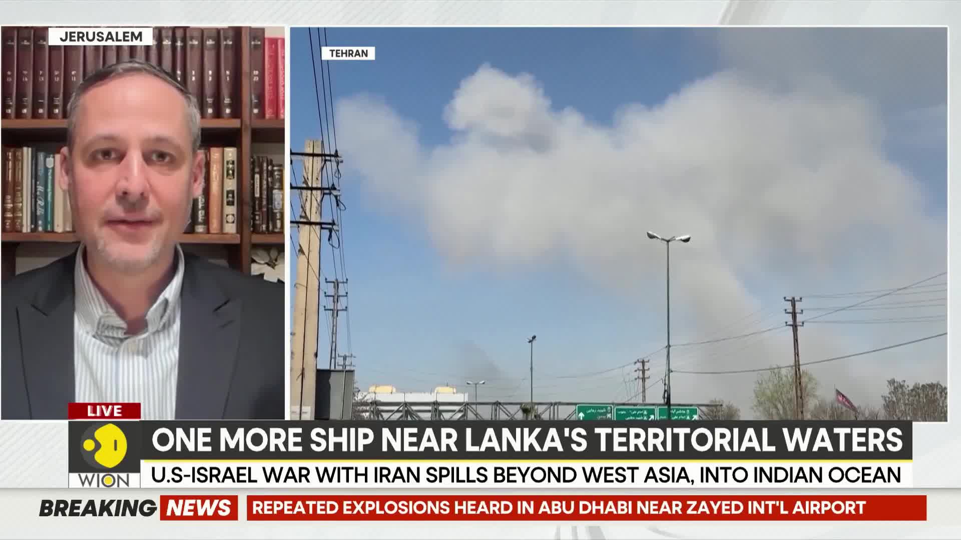 Thick plumes of smoke rise into the sky from what appears to be an industrial area in Tehran. Overhead power lines crisscross the frame, silhouetted against the hazy blue.