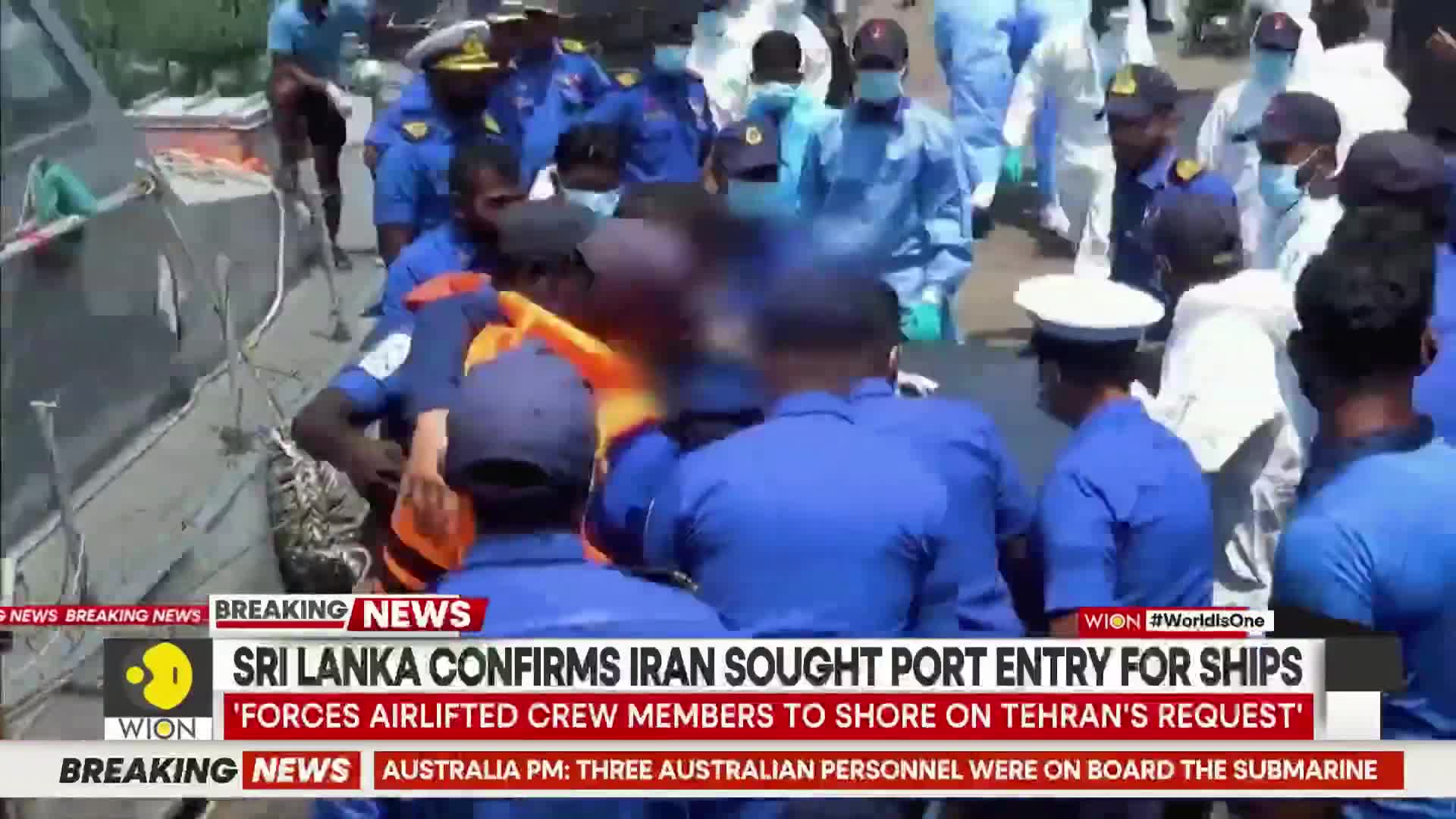 Men in blue uniforms are helping someone in an orange vest off a boat. Others in white hazmat suits stand nearby.