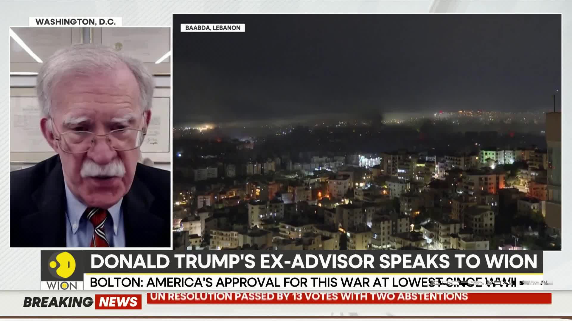 A man in a suit speaks from Washington, D.C. while a nighttime cityscape of Baabda, Lebanon, glows with lights and smoke plumes rise in the distance.