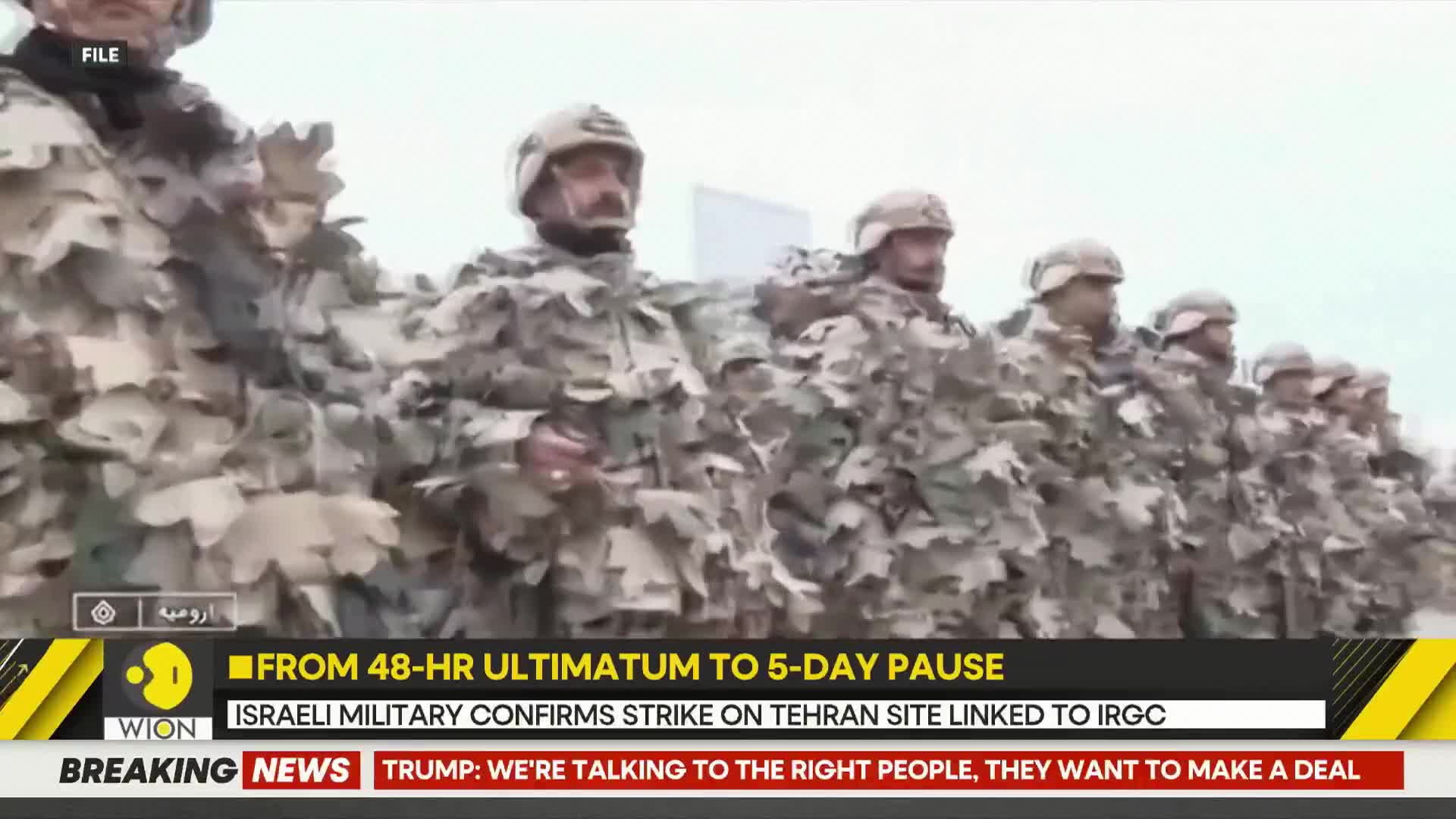 A line of soldiers in camouflage stands at attention, their helmets and rifles visible. A news ticker at the bottom of the screen reports on an Israeli military strike.