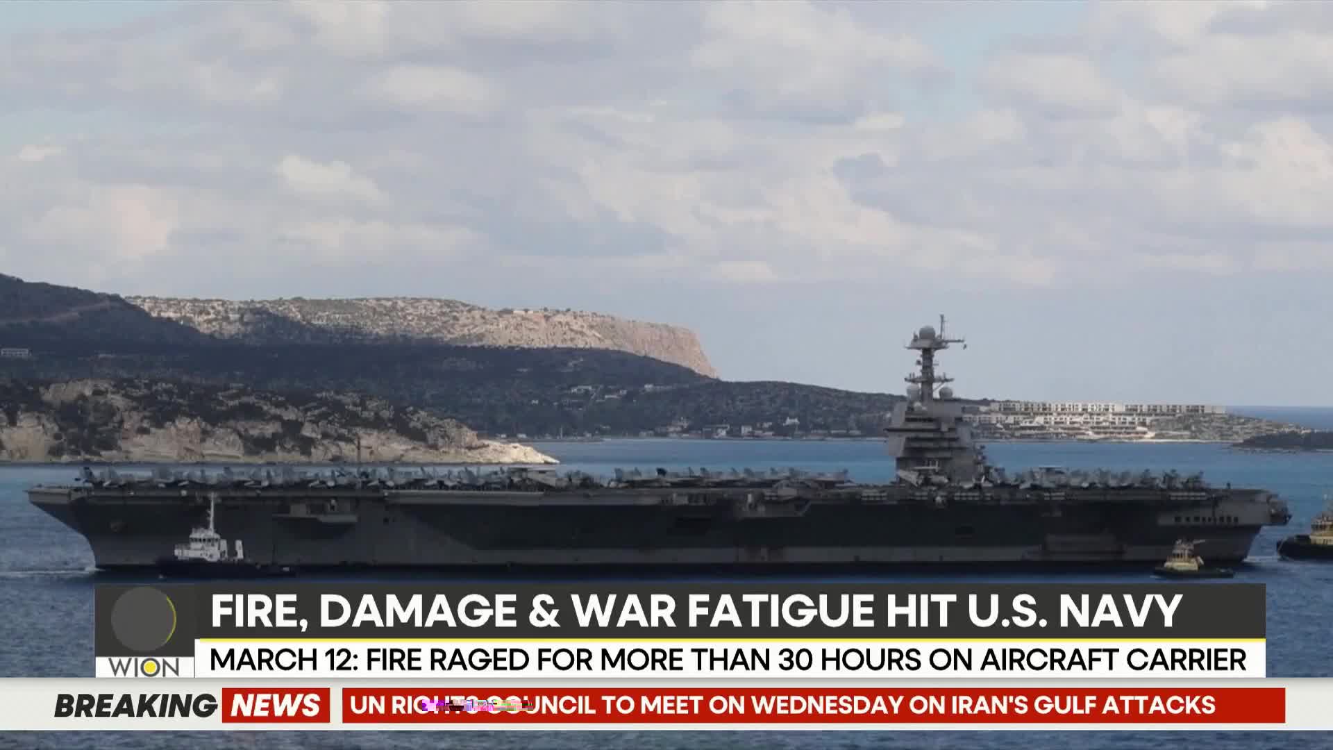 A large aircraft carrier glides through the water, dwarfed by a mountainous coastline. A small tugboat escorts the carrier, its wake rippling behind it.