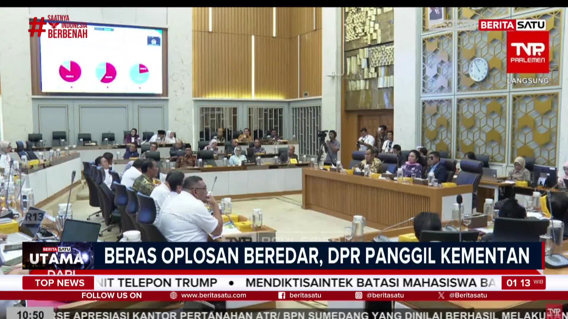 A parliamentary session is underway in Indonesia, with a large screen displaying charts and graphs. The BeritaSatu English news ticker indicates the topic is "rice mixing" and the calling of the ministry.
