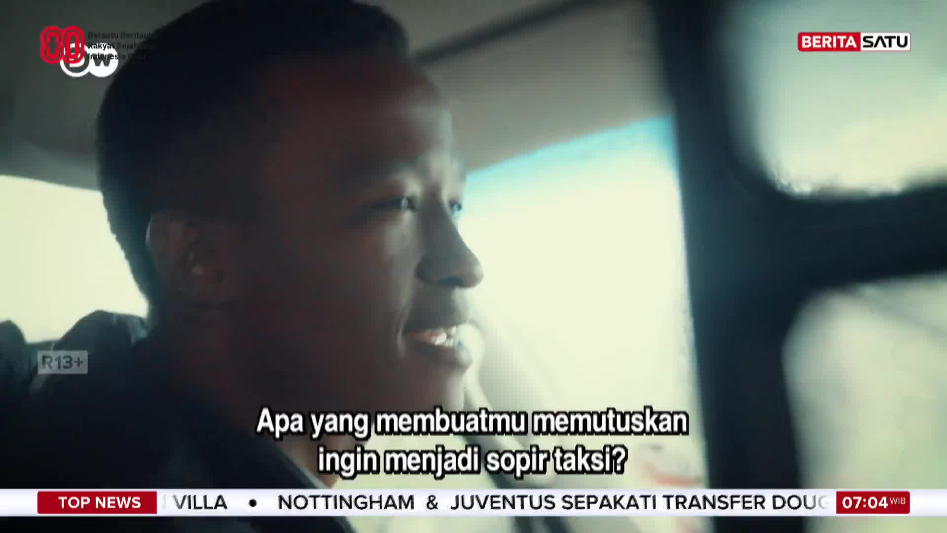 A man is being interviewed inside a car, his face lit by the interior light. Below, the BeritaSatu English logo is visible, along with text in Bahasa Indonesia.
