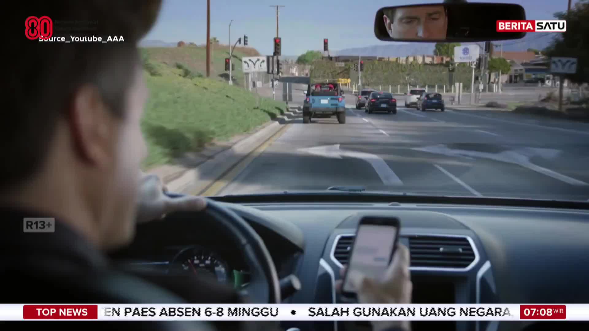 A driver, seen from behind the wheel, is glancing at their phone while other cars move ahead on the road. The news banner at the bottom, likely from BeritaSatu English, displays headlines in Indonesian.
