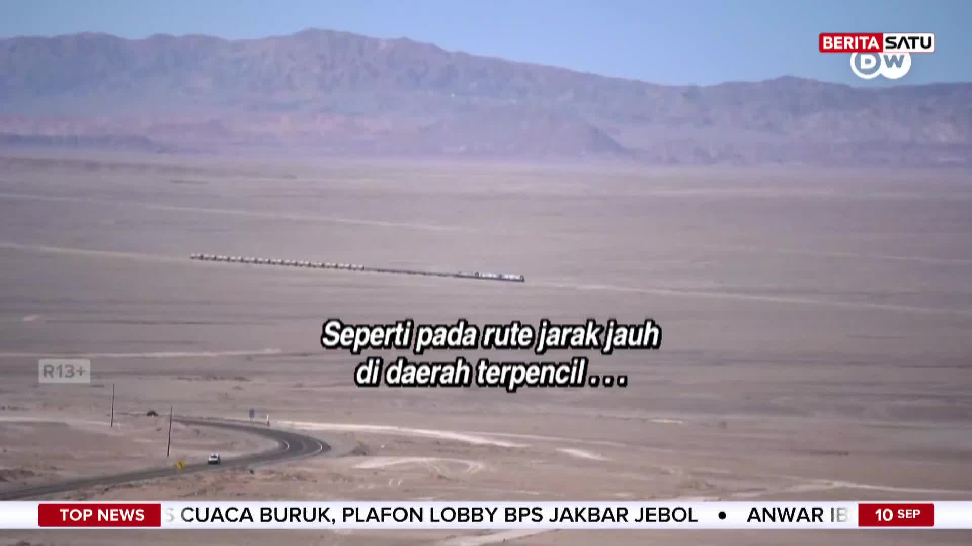 A long line of vehicles travels across a vast, arid landscape, seemingly headed towards distant mountains. The BeritaSatu English broadcast covers the scene, highlighting the remote location.
