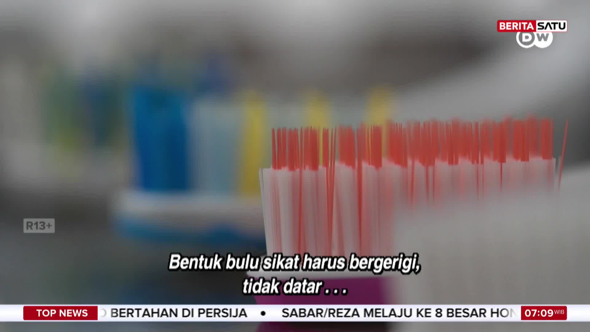 A close-up of a toothbrush head shows its red-tipped bristles, with others blurred in the background. The BeritaSatu English broadcast from Indonesia is discussing toothbrush features.
