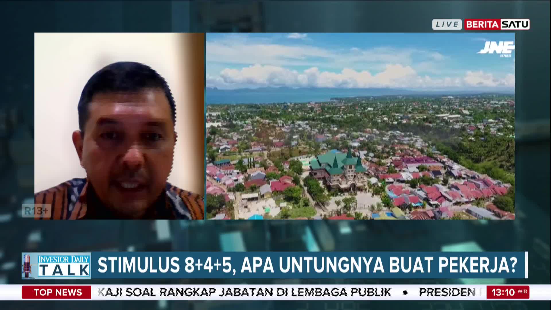 A man speaks earnestly on the screen, while a wide shot of a coastal Indonesian town plays behind him on BeritaSatu English. The broadcast is discussing stimulus packages for workers.
