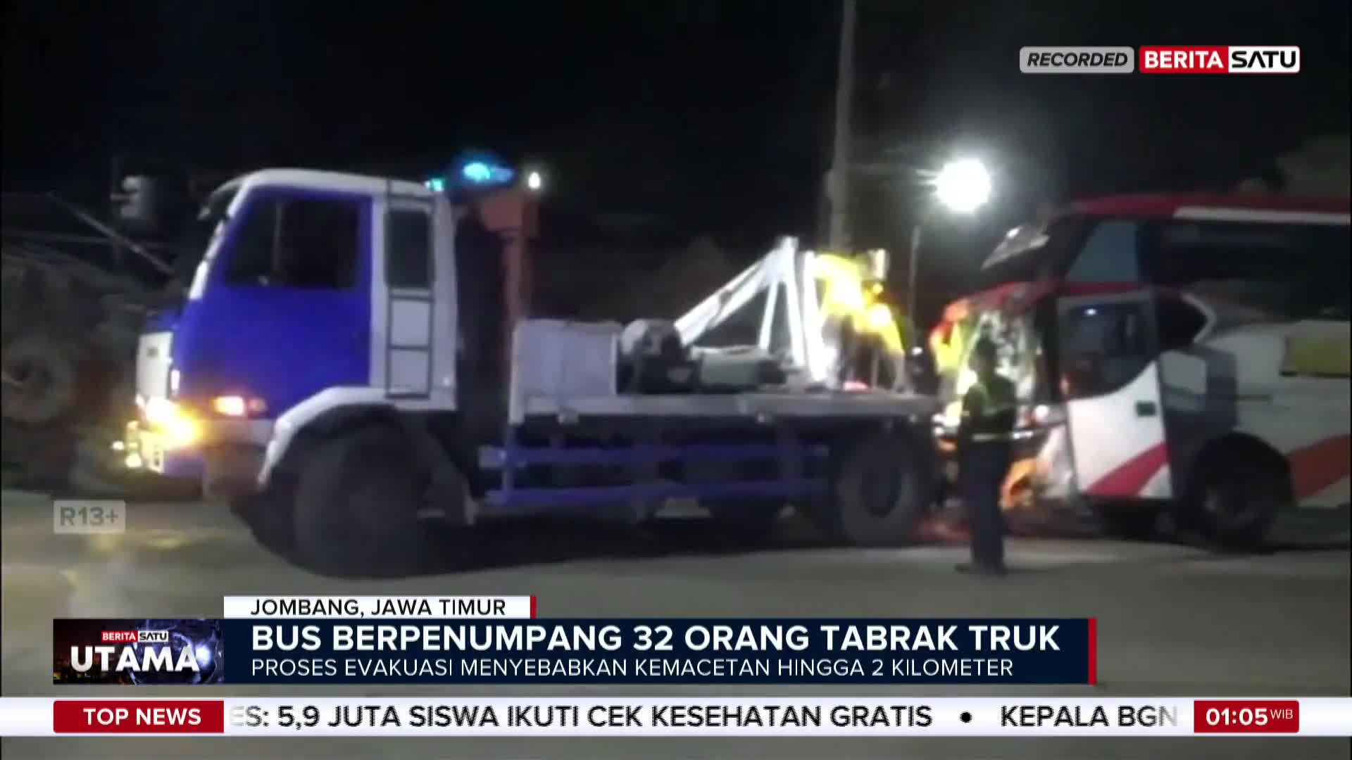 A tow truck, its blue and white cab lit up, is positioned near a damaged bus.  Emergency personnel in yellow vests are visible, likely assessing the scene of a collision, as reported by BeritaSatu English.
