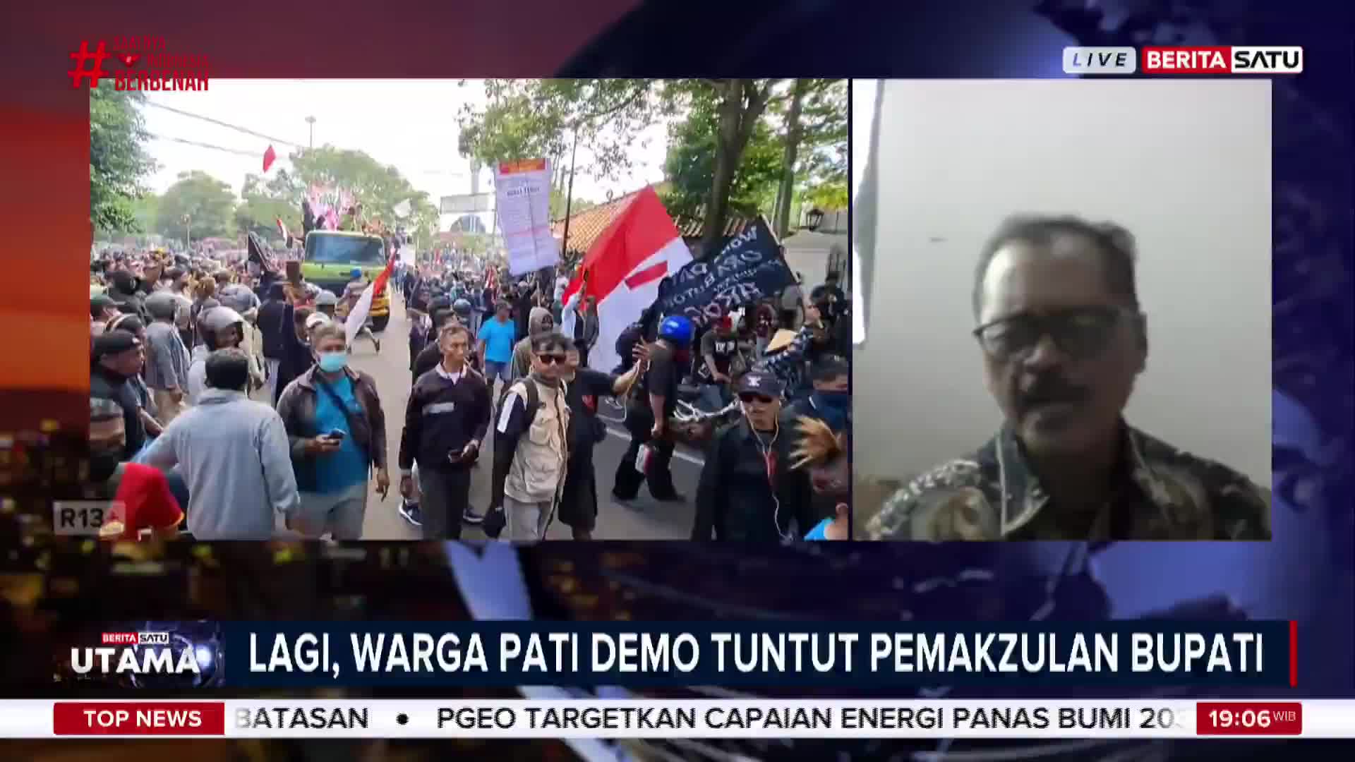 A crowd in Indonesia marches down a street, carrying banners and flags. A man in glasses is speaking on a live BeritaSatu English broadcast about the demonstration.
