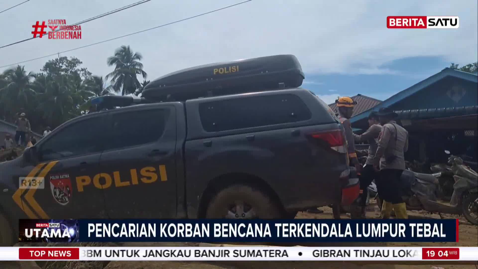 A dark police truck is parked, its roof carrier labeled "POLISI." Several officers in uniform are standing near a damaged building, part of a scene covered by BeritaSatu English news about the search for victims of a disaster in Indonesia.
