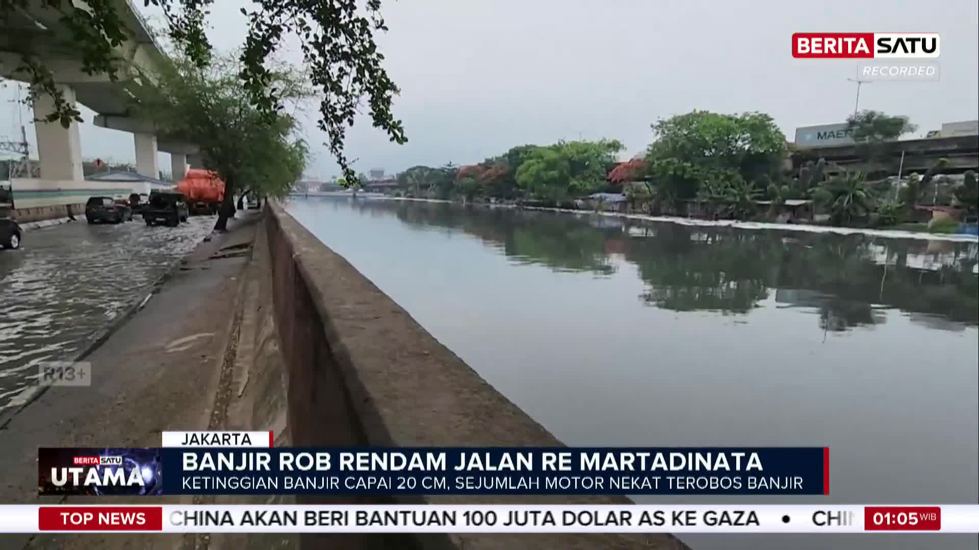 The road beside the river is flooded, with cars and trucks partially submerged. The BeritaSatu English broadcast reports on the flooding in Jakarta, Indonesia.
