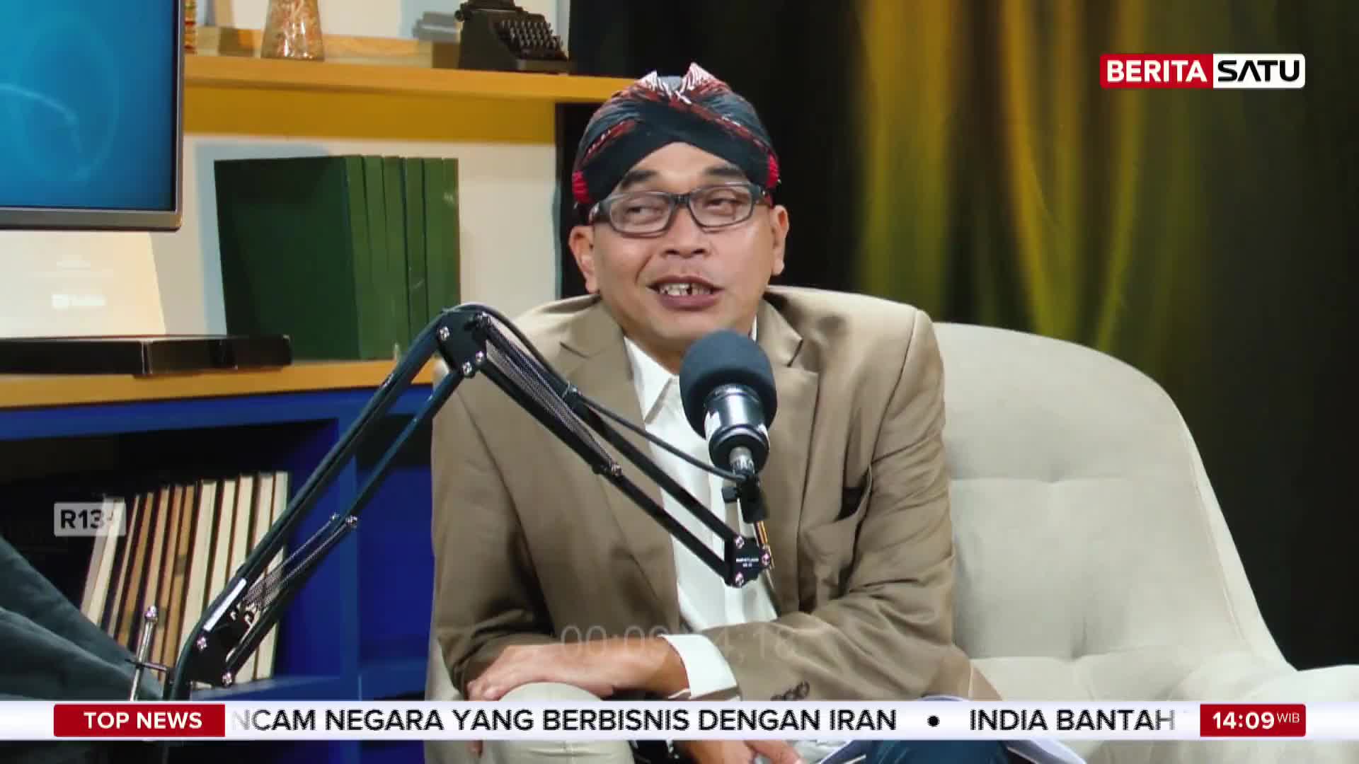 A man in a tan suit and a patterned head covering speaks into a microphone. The BeritaSatu logo is visible in the upper right corner.