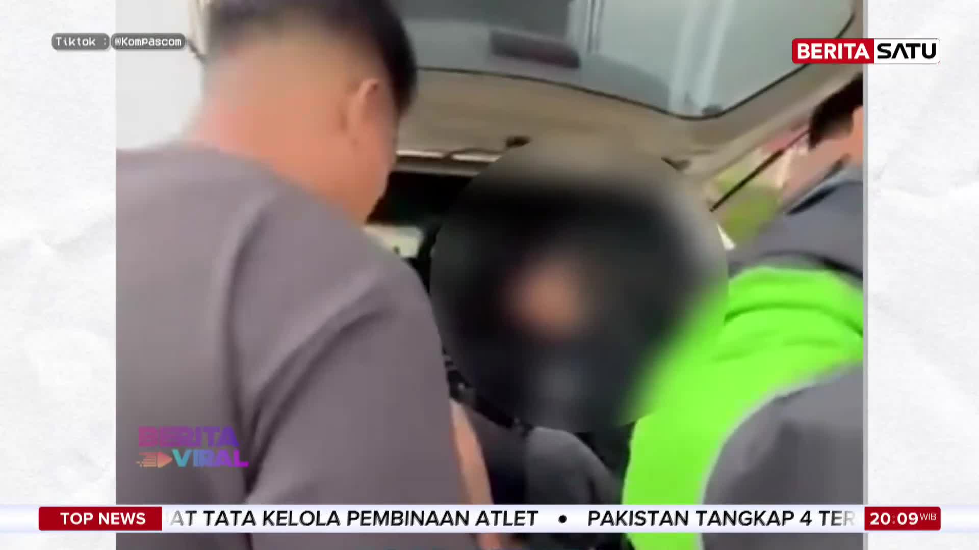 A man in a grey shirt helps guide someone wearing a black helmet into the back of a vehicle. Another person in a bright green jacket is visible behind them.