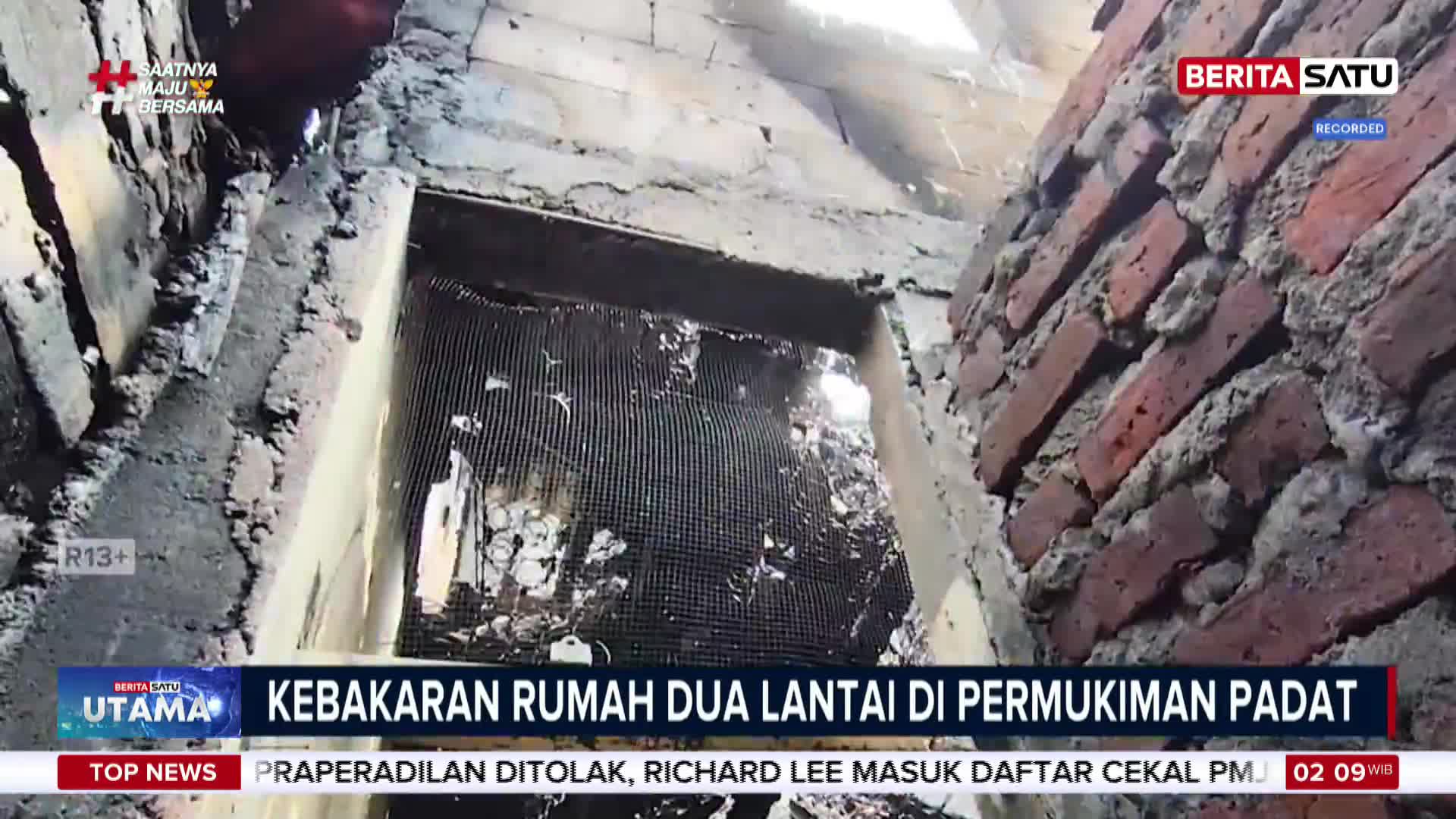 The charred remains of a two-story house are visible through a broken window. Debris litters the floor inside, and the brick walls show signs of intense heat.