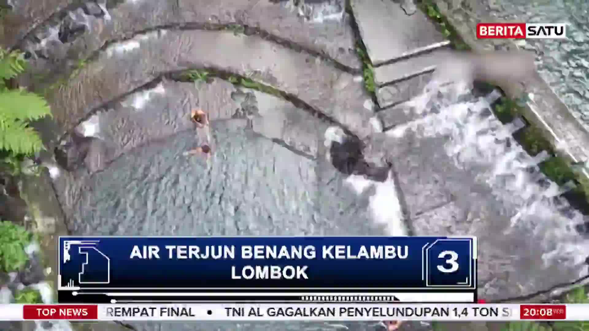 Two people are wading through the tiered pools of Benang Kelambu waterfall in Lombok, Indonesia. The water cascades down the stone steps, creating a lively scene.