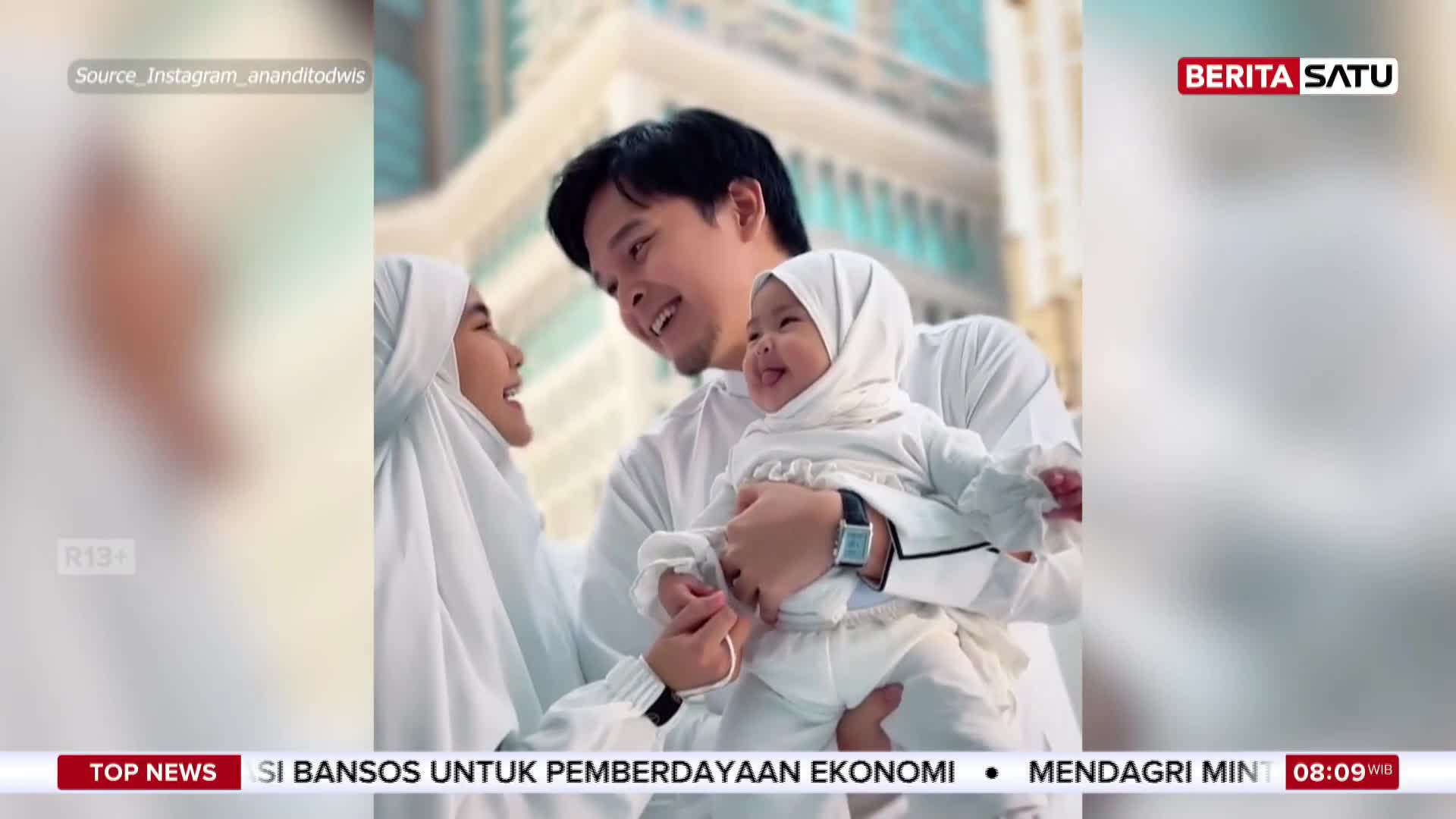 A man holds a laughing baby, while a woman looks on, all dressed in white. This family moment is featured on BeritaSatu English.