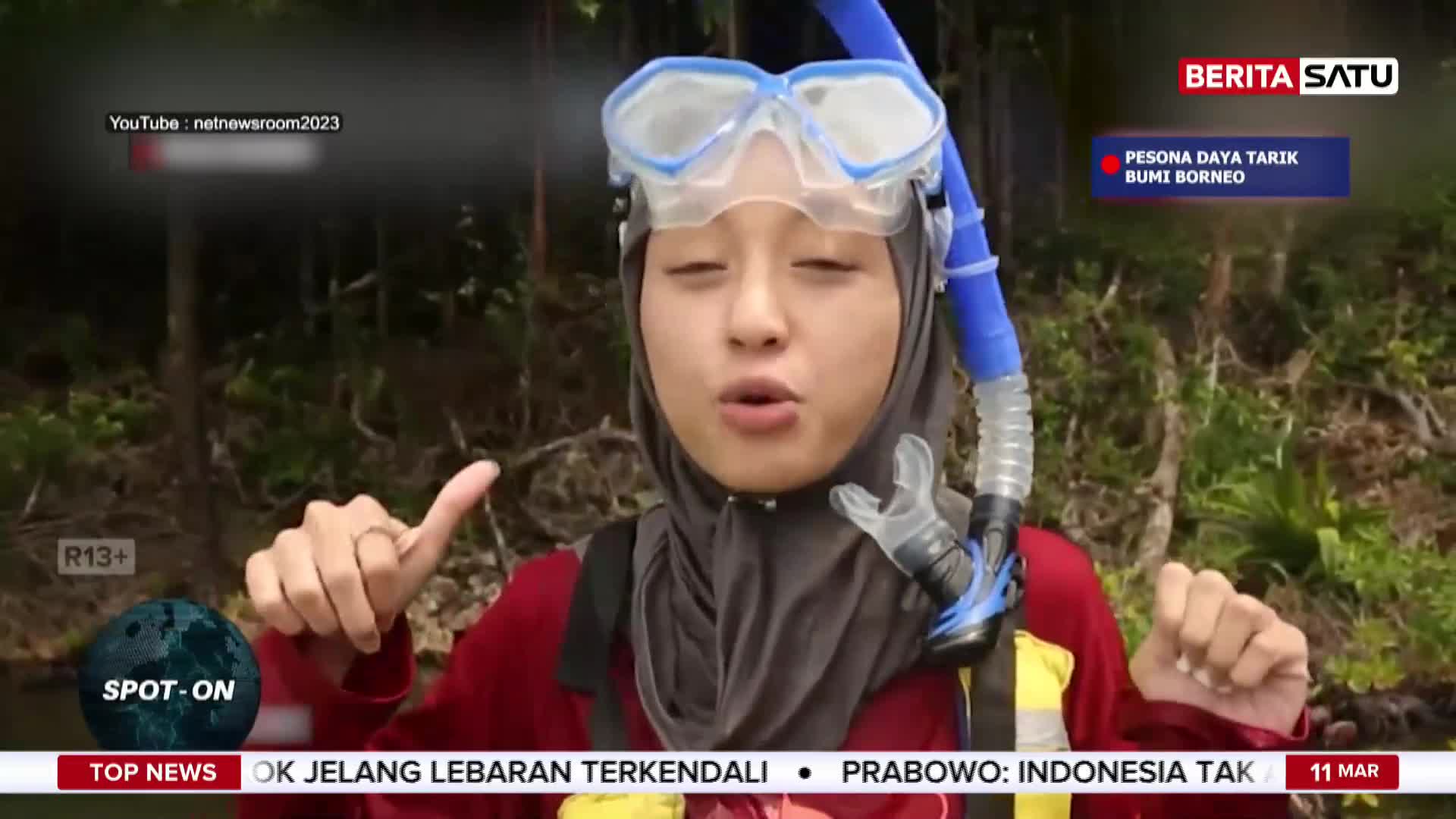 A young woman in a hijab and snorkeling gear gestures as she speaks, likely for a BeritaSatu report on Borneo's natural attractions. The lush green foliage behind her suggests an outdoor setting in Indonesia.