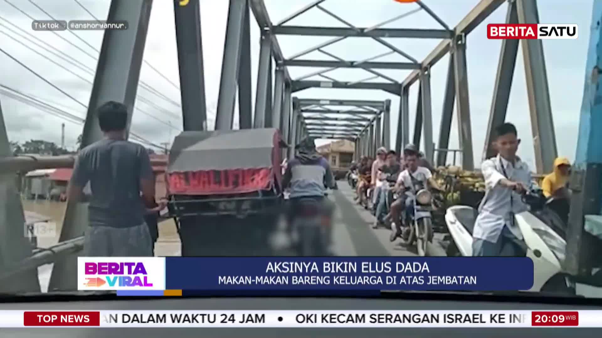 A line of motorcycles, some carrying multiple passengers, inches across a narrow bridge. A truck ahead of them is stopped, its brake lights glowing red.