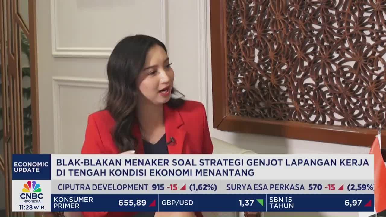 A woman in a red blazer speaks animatedly, framed by a decorative wooden panel. The CNBC Indonesia logo and financial data are displayed on the screen below.
