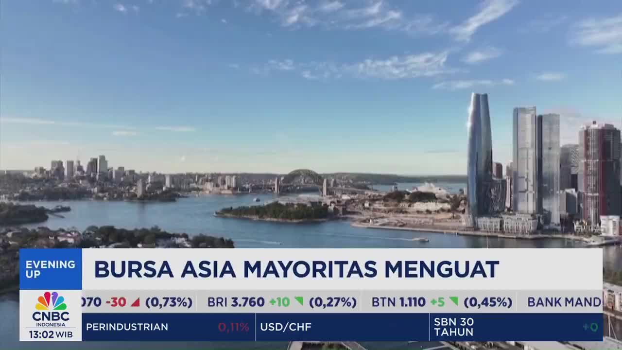 The CNBC Indonesia broadcast shows a cityscape with a bright blue sky. Below the view, market data scrolls across the screen, reporting on Asian stocks.
