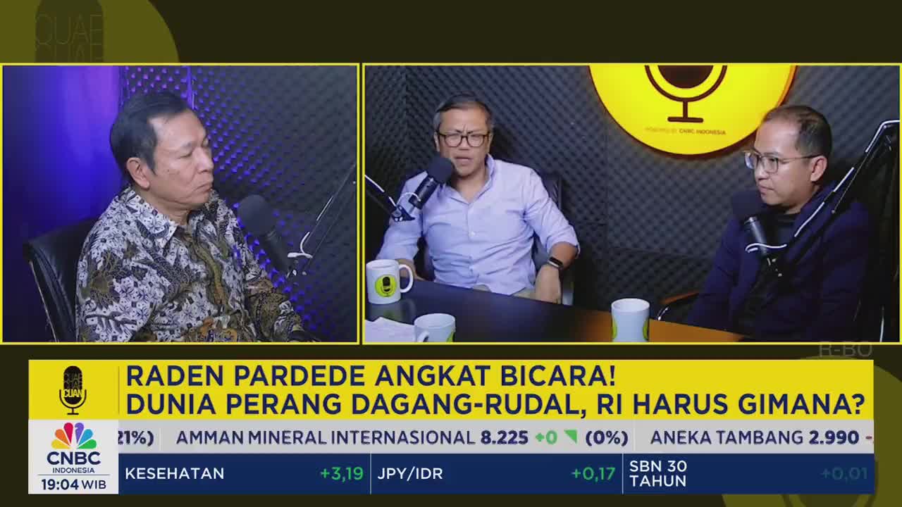 Three men sit at a table, each with a microphone, engaged in a discussion on a CNBC Indonesia program. The man in the center gestures with his hands as he speaks.

