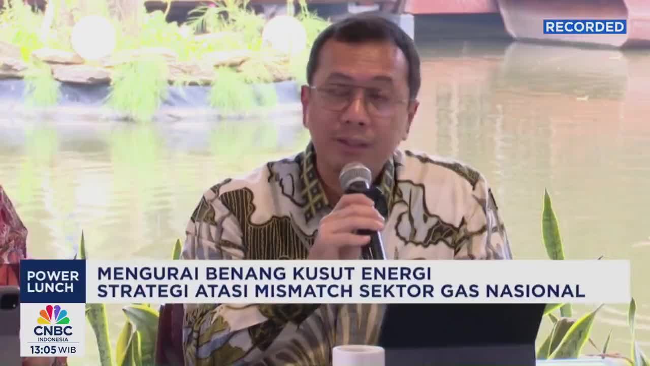 A man in a patterned shirt speaks into a microphone, likely discussing energy strategy on CNBC Indonesia. Behind him, a serene water feature provides a backdrop for the "Power Lunch" broadcast.
