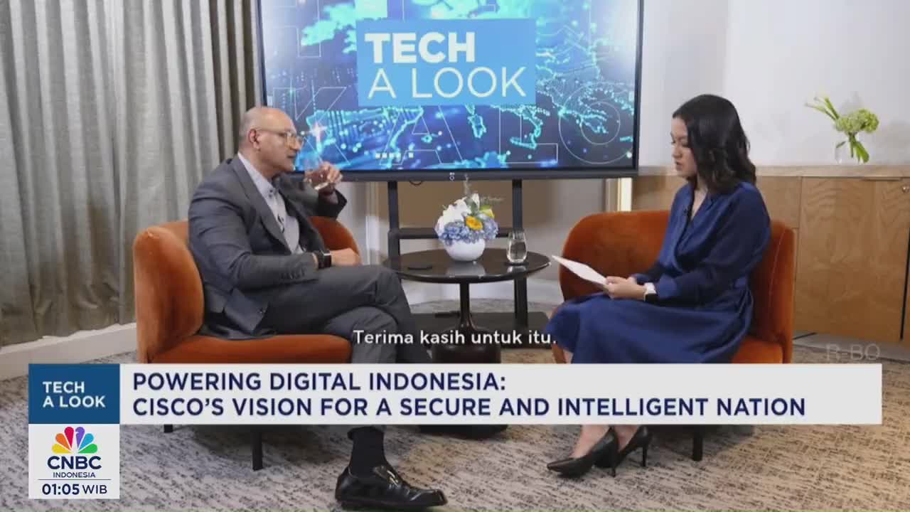 A man in a suit gestures while speaking, seated across from a woman in a blue dress holding papers. The CNBC Indonesia logo anchors the lower left corner, and the backdrop reads "Tech A Look."

