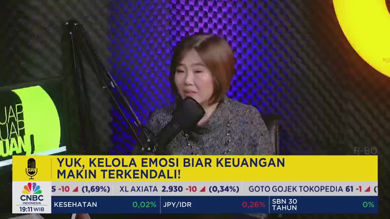 A woman speaks into a microphone, her face lit by the studio lights. The CNBC Indonesia logo and financial data are displayed at the bottom of the screen.
