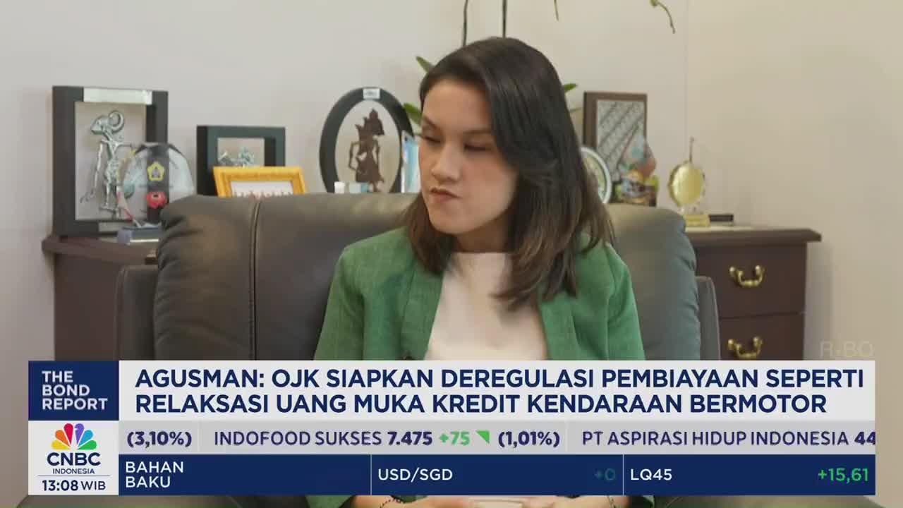 A woman in a green blazer sits on a dark leather couch, speaking into the camera on CNBC Indonesia. The lower third of the screen displays financial news, with the headline mentioning OJK and credit for motor vehicles.
