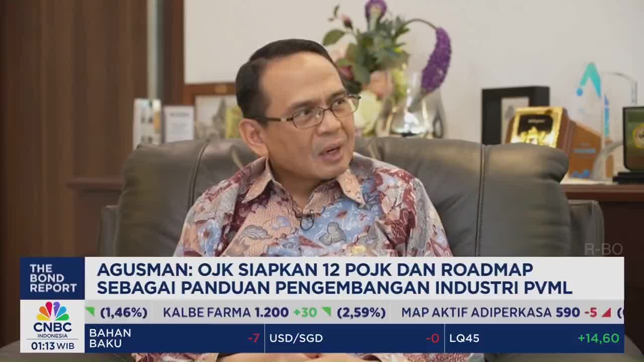 A man in glasses and a patterned shirt speaks, gesturing with his hands. Below, a CNBC Indonesia graphic displays financial data and the headline "AGUSMAN: OJK SIAPKAN 12 POJK DAN ROADMAP."
