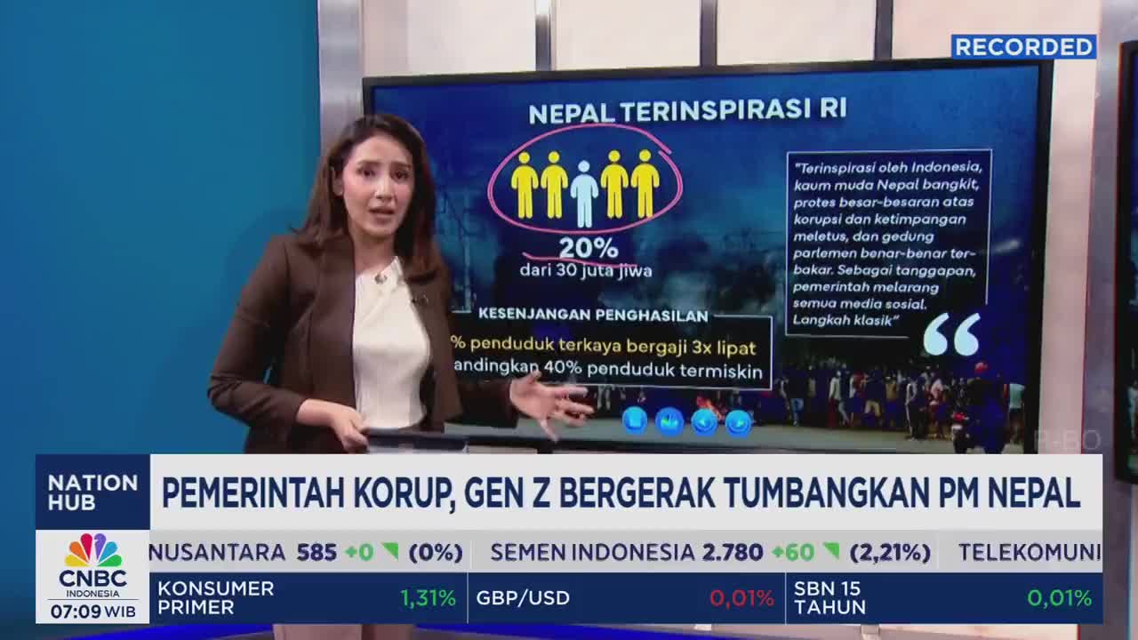A woman in a brown blazer stands in front of a large screen, gesturing towards a graphic about Nepal on CNBC Indonesia. The screen displays information about protests and income inequality, with text in Indonesian.
