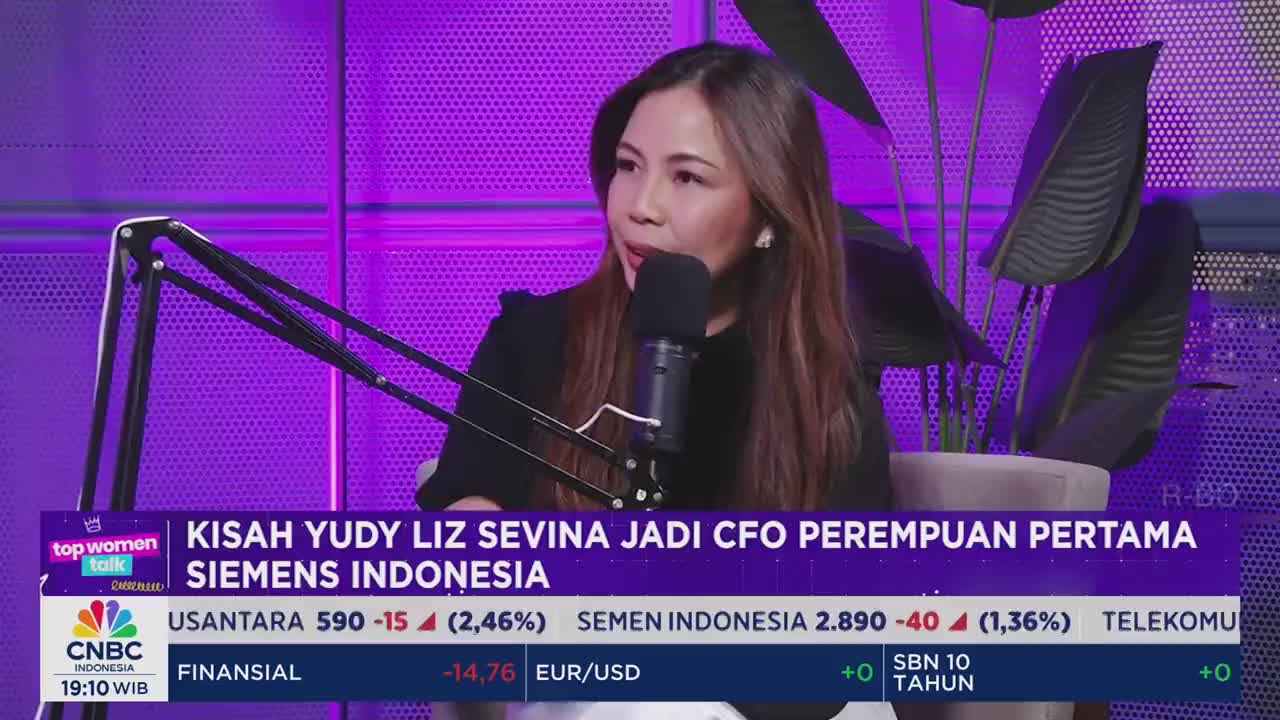 A woman is speaking into a microphone, her face illuminated by the studio lights of CNBC Indonesia. The screen displays financial data and the headline "KISAH YUDY LIZ SEVINA JADI CFO PEREMPUAN PERTAMA SIEMENS INDONESIA."
