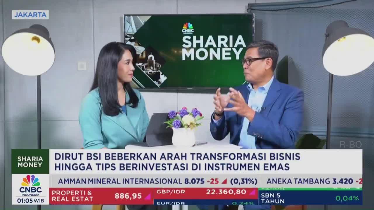 A woman in a teal top listens intently as a man in a blue suit gestures with his hands. The CNBC Indonesia "Sharia Money" segment is underway, with financial data displayed below.
