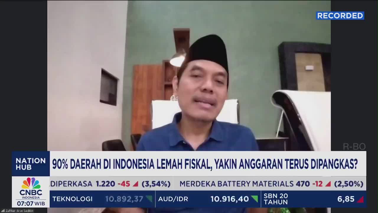 A man in a black cap speaks directly into a camera, likely for a CNBC Indonesia broadcast. Below him, the screen displays financial data and a headline about fiscal weakness in Indonesia.
