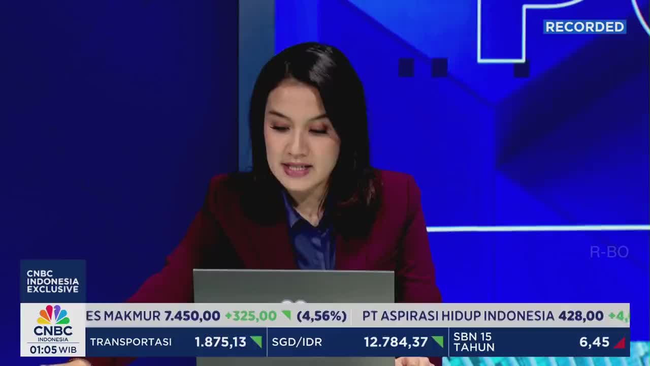 A woman in a maroon blazer reads from a laptop, speaking on CNBC Indonesia. Below her, stock market data scrolls across the screen.
A woman in a maroon blazer reads from a laptop, speaking on CNBC Indonesia. Below her, stock market data scrolls across the screen.