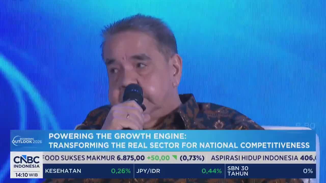A man in a batik shirt speaks into a microphone on a stage. Below him, a CNBC Indonesia ticker displays stock market data.