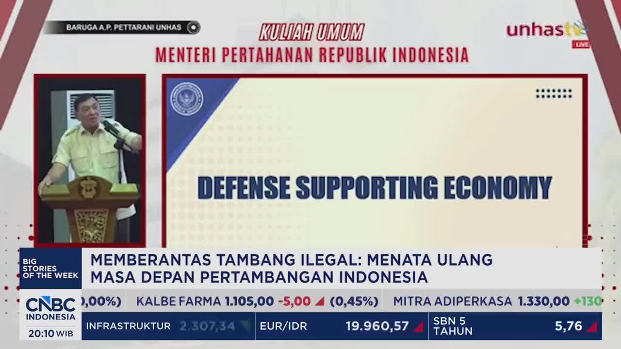 The Indonesian Minister of Defense stands at a podium, gesturing as he speaks. A large screen behind him displays "DEFENSE SUPPORTING ECONOMY" in bold letters.