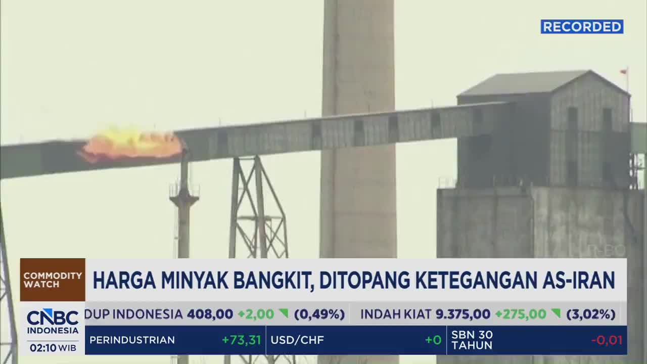 A plume of bright orange flame erupts from a conveyor belt system at an industrial facility. The CNBC Indonesia broadcast overlay indicates this is related to rising oil prices.