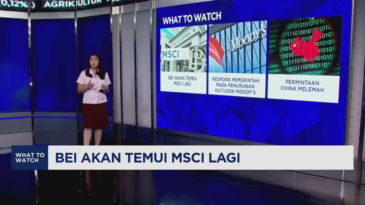 A woman stands on a studio floor, gesturing towards a large screen displaying news headlines. The screen shows a graphic with the MSCI logo and text in Indonesian, alongside other financial news items.