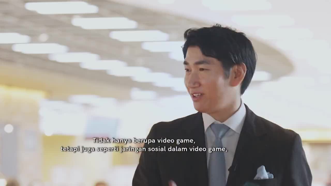 A man in a suit speaks, his words appearing as text on screen. The backdrop is bright and modern, hinting at a professional setting in Indonesia.